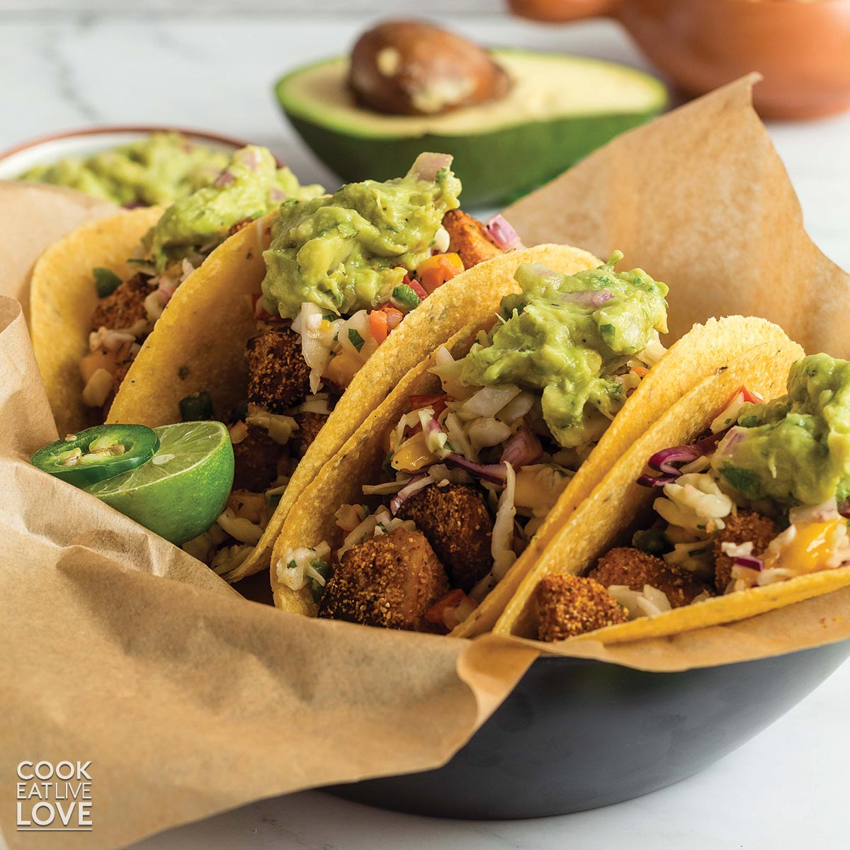 Basket of crispy vegan fish tacos topped with guacamole.