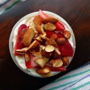 Oat and Yogurt Parfait topped with almonds and strawberries on dark brown cutting board.