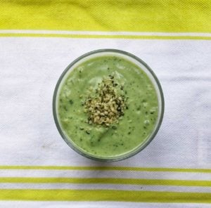 Green smoothie with spinach pictured in glass on tea towel. Garnished with hemp seeds.