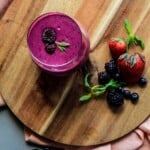 Glass of beetroot smoothie surrounded by berries on a cutting board