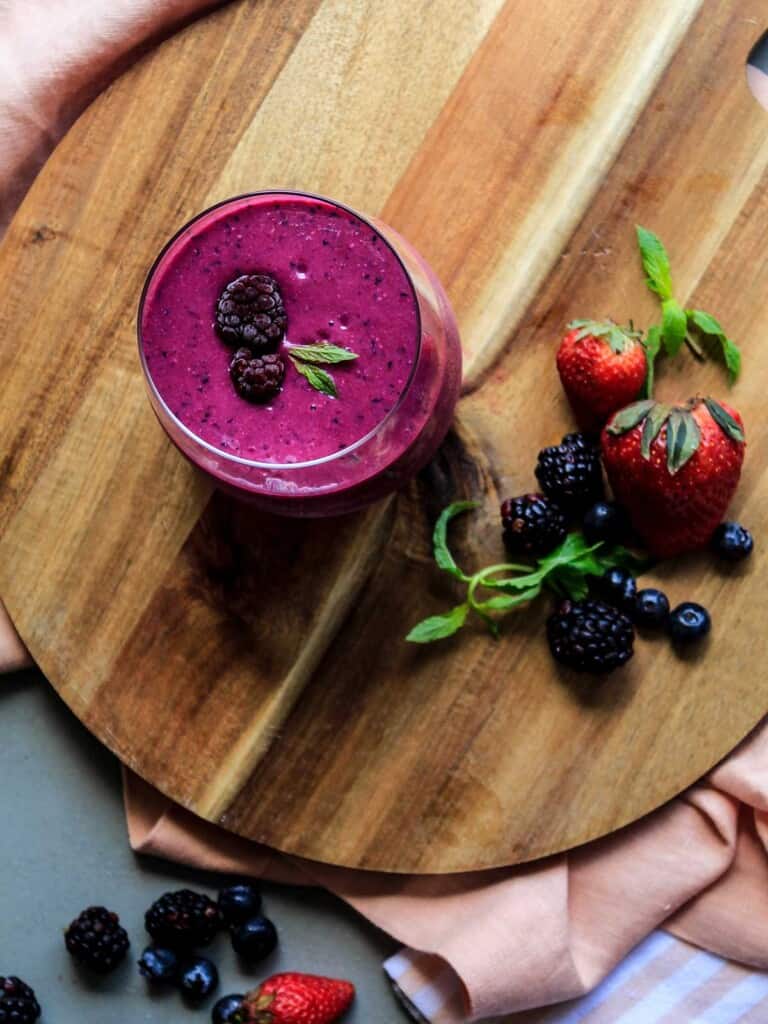 Glass of beetroot smoothie surrounded by berries on a cutting board