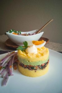 Layered causa on white plate with salsa criolla on side.