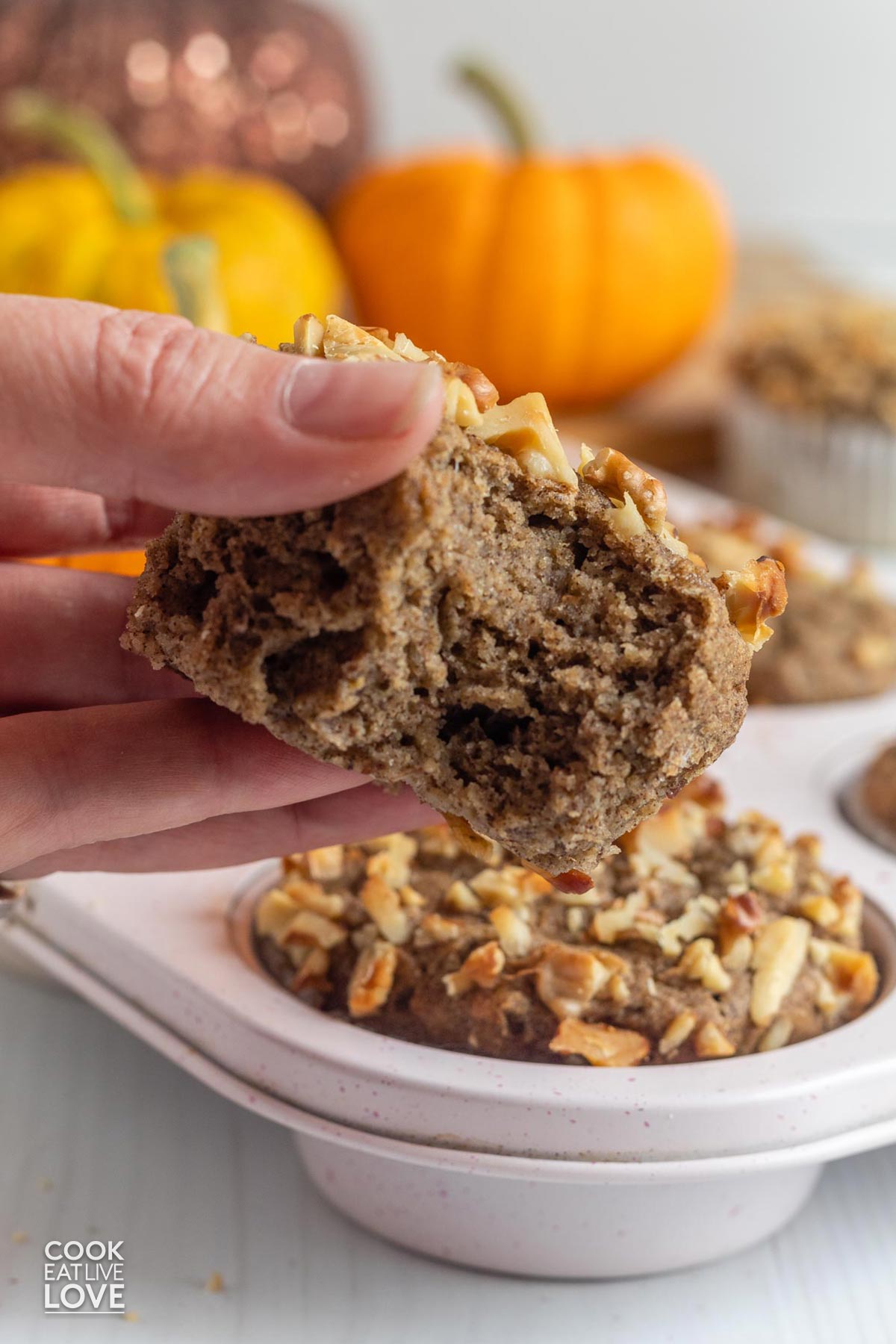A hand holding up a vegan pumpkin muffin with banana to see the inside.