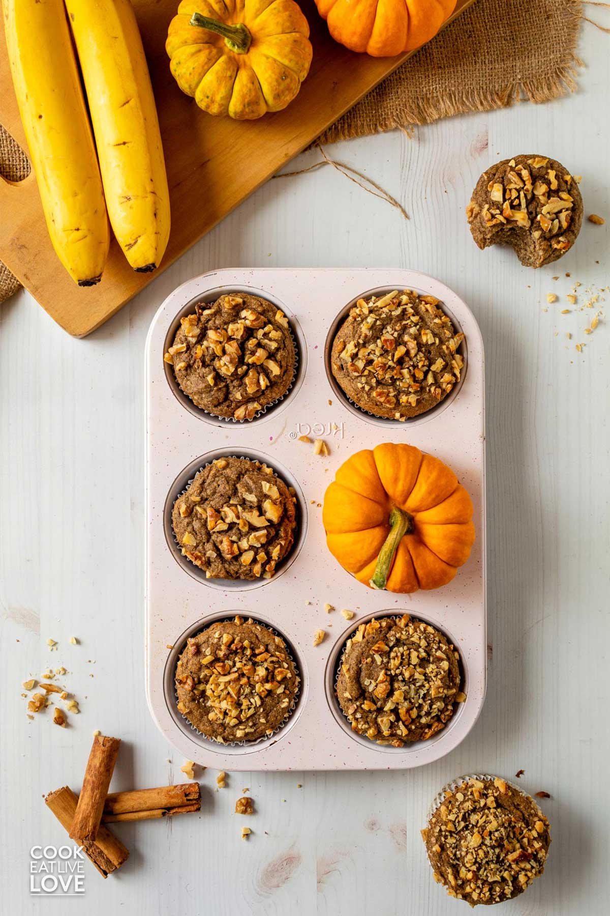 Fresh baked eggless pumpkin muffins in a muffin pan with a small pumpkin in one of the muffin openings.
