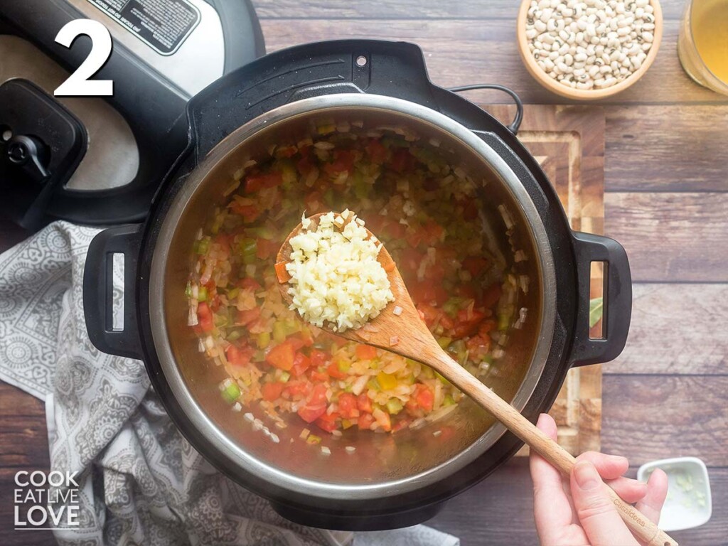 Adding garlic to the vegetables for vegan black eyed peas.