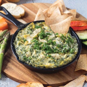 Vegan spinach dip in a cast iron skillet with tortilla chips and vegetables.