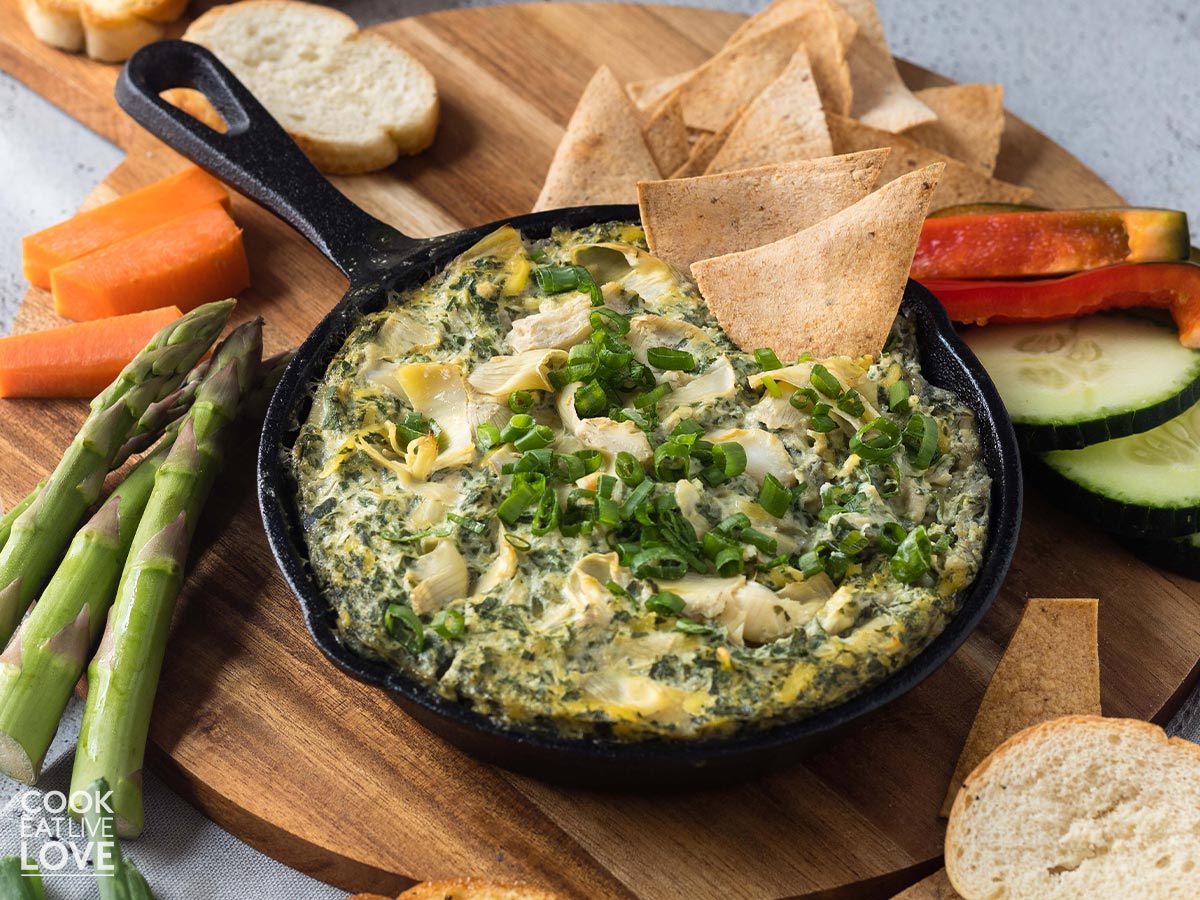 Dairy free spinach artichoke dip in cast iron skillet with chips and veggies.