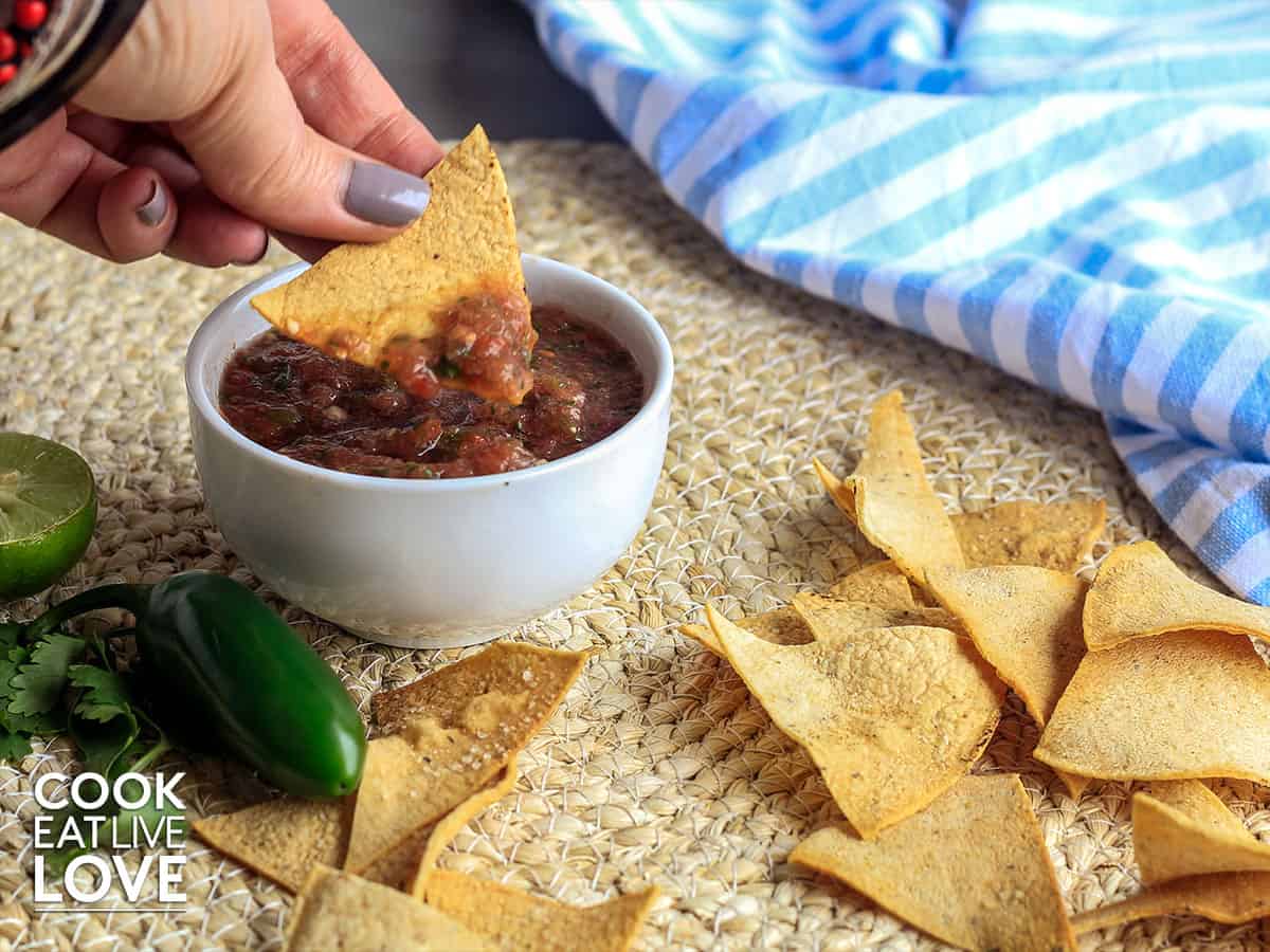 Salsa in bowl with hand dipping a chip