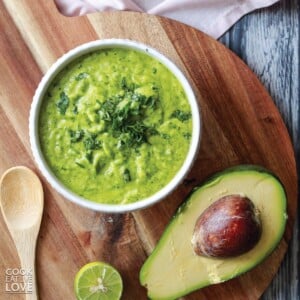 Guasacaca sauce in white bowl on a cutting board with avocado half, limes and cilantro.