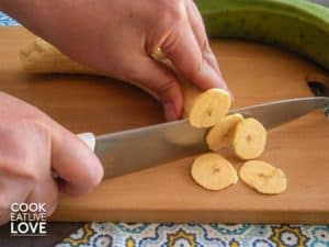 Plantains are shown being sliced by hand with a sharp knife.