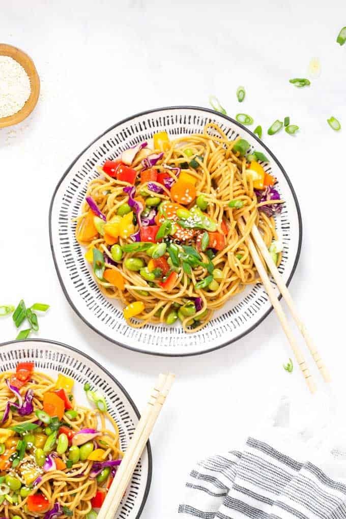 White and blue plate with noodle salad accompanied by wooden chopsticks.