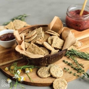Okara crackers in a bowl on a cutting board with fresh herbs