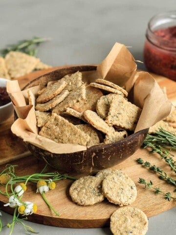 Okara crackers in a bowl on a cutting board with fresh herbs