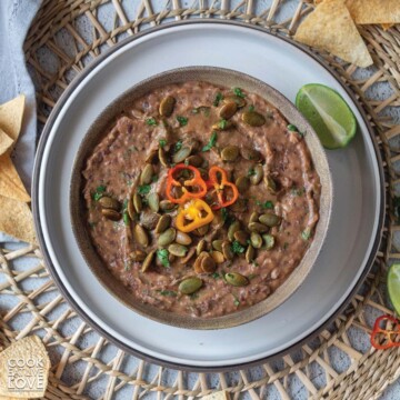 Bowl of vegan black bean dip on plate with chips and lime.