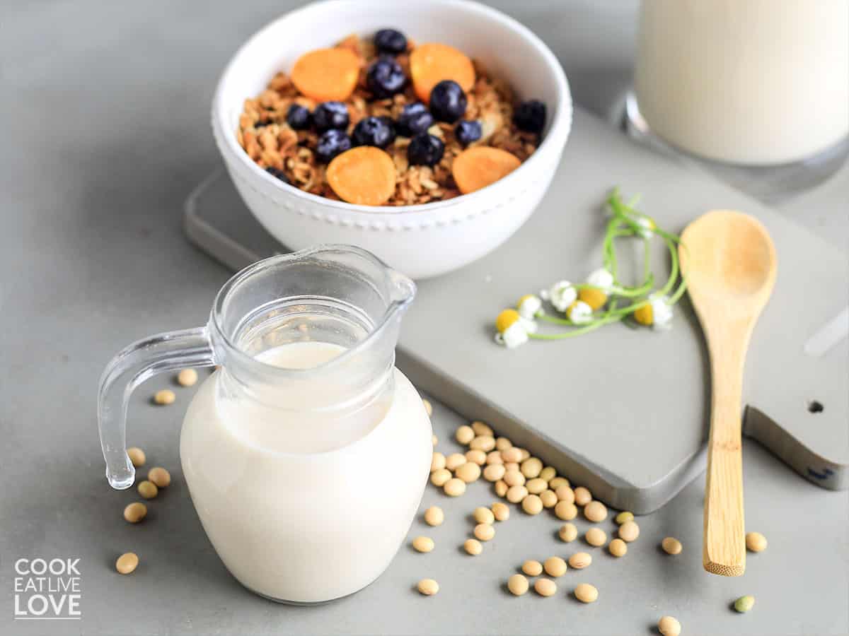 Soy milk in a pitcher with bowl of granola in back