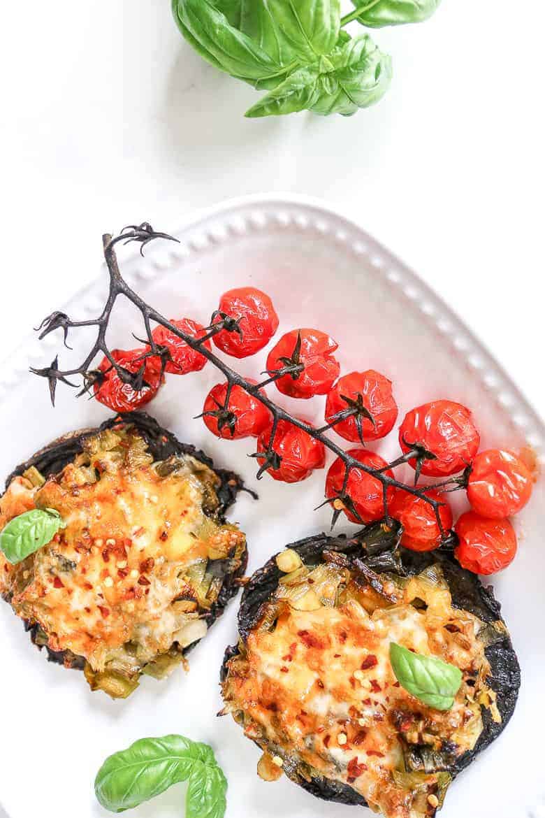 Portobello pizzas on white plate on white background. Garnished with roasted tomatoes on stem.
