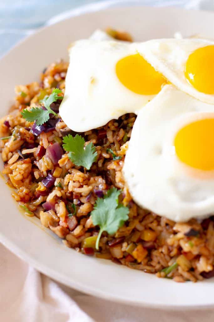 Closeup of bowl of fried rice topped with three sunny side up eggs.