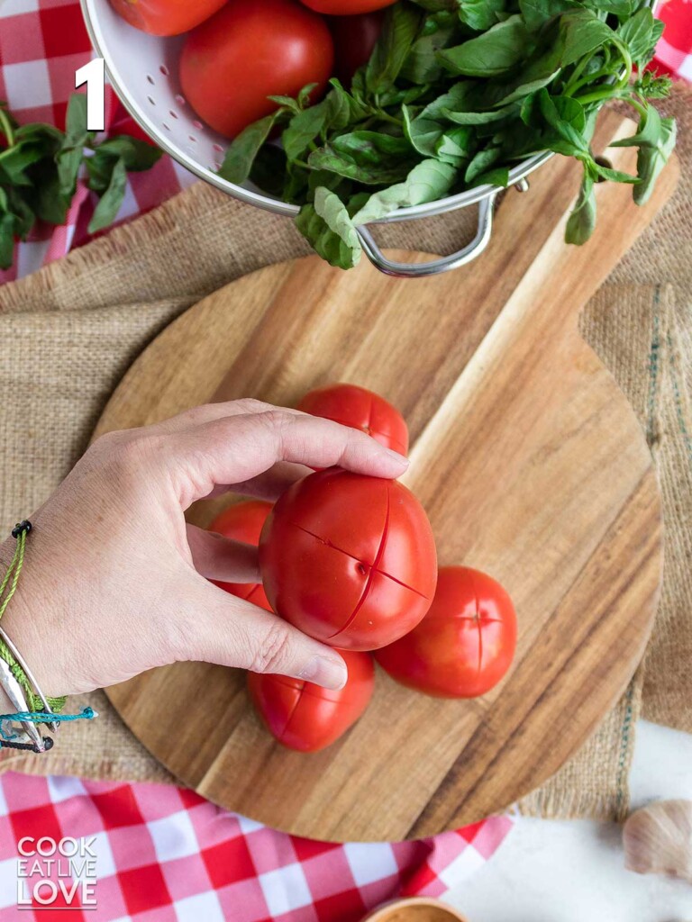 Handing holding a tomato with an X cut into the bottom.