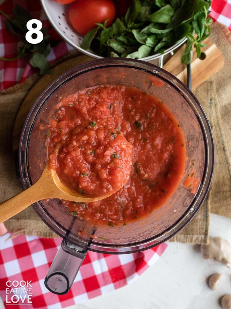 Spoonful of fresh tomato pizza sauce up over the bowl of the food processor.