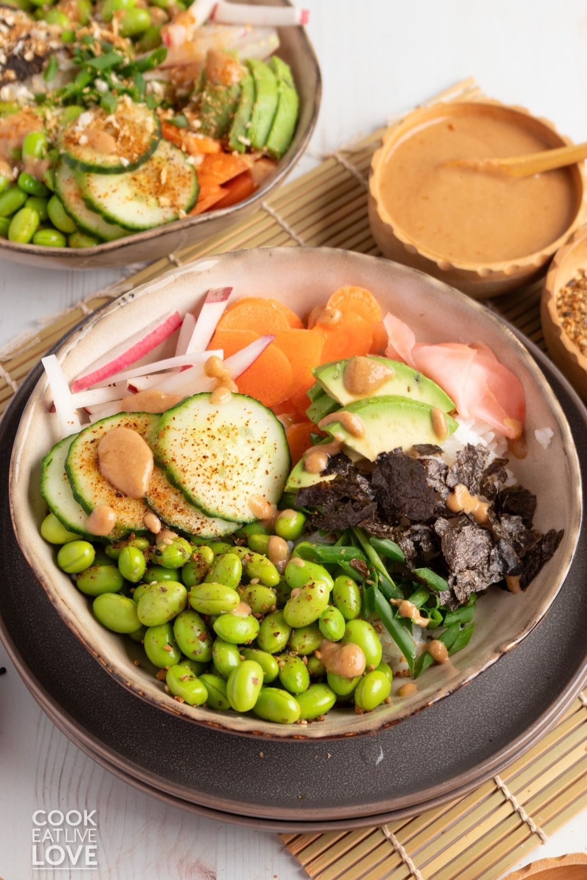 Two vegan sushi bowls on a table with sauces.