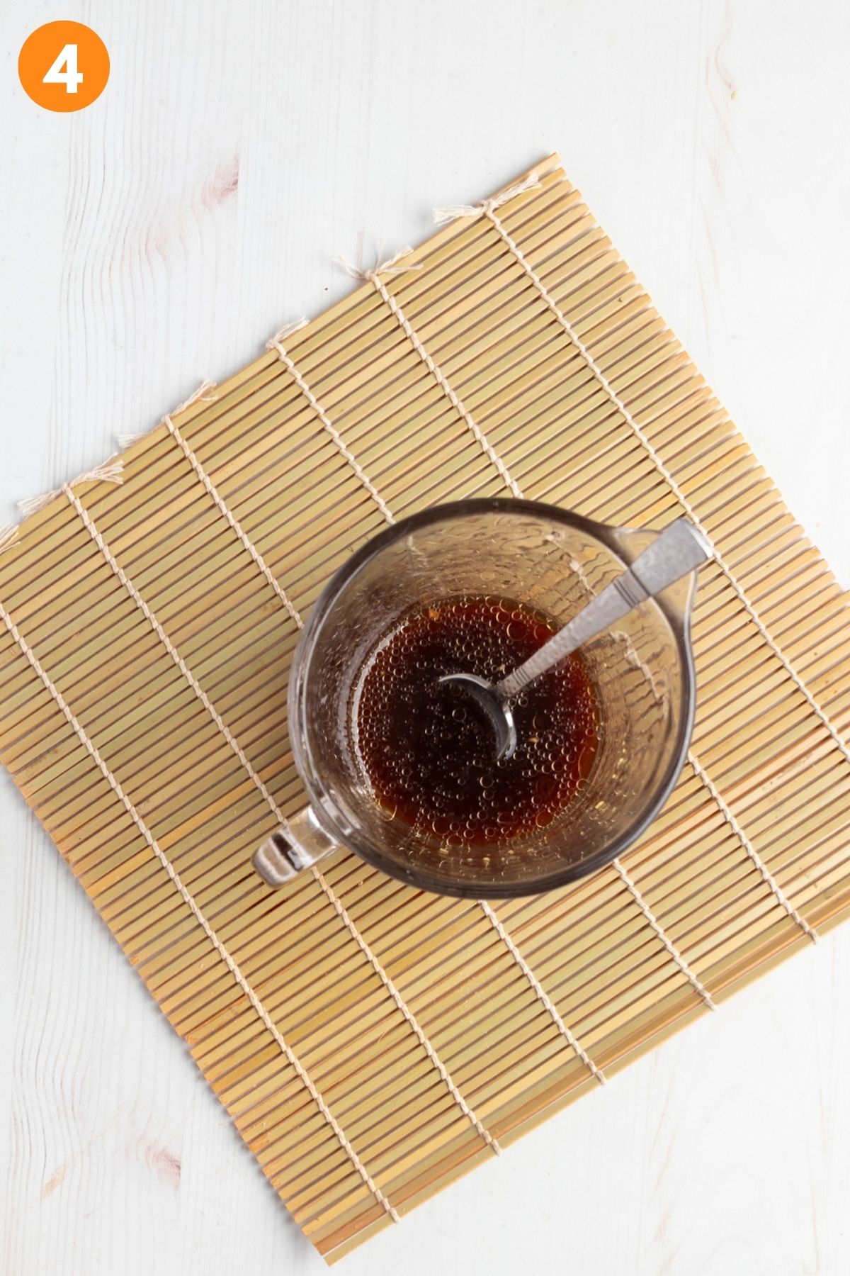 Soy sauce mixture in a glass container with a small whisk. 