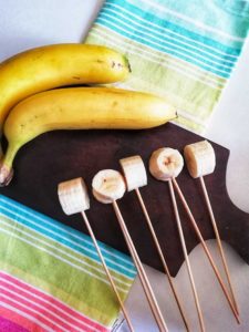 Bananas are shown cut into pieces and skewers are inserted.