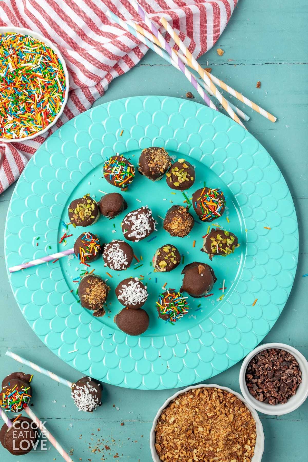 Chocolate covered bananas on a aqua plate with sprinkles to the sides and straws.