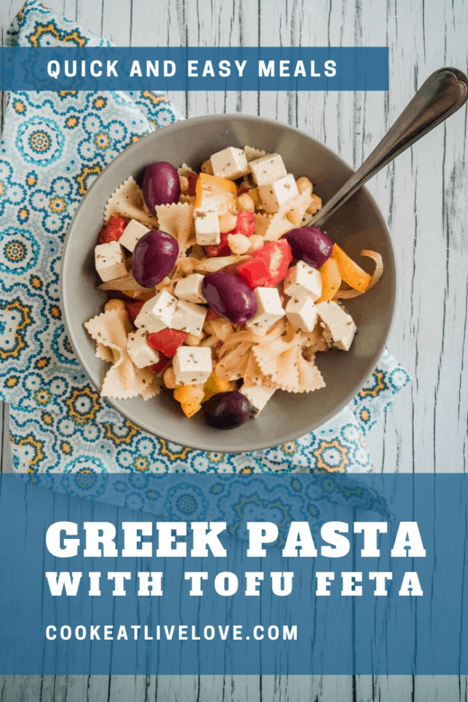 Greek pasta with tofu feta is ready to eat and enjoy. Served up in dark gray bowl on white wood background.
