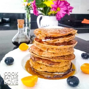 A plate topped with a vase of flowers on a table and plate of stacked pancakes