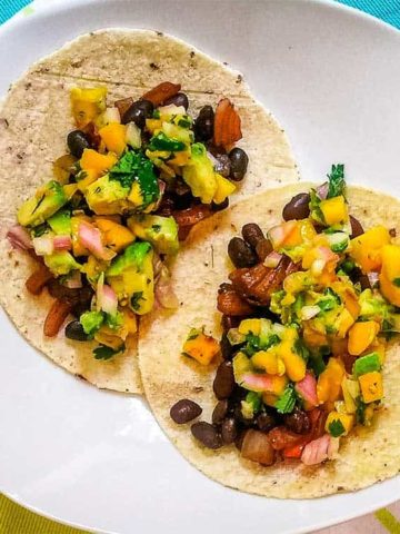 Black bean and mango tacos ready to eat on white plate.