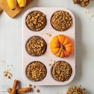 Eggless pumpkin muffins with banana in a muffin pan with a mini pumpkin.