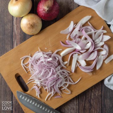 Overhead photo of red onion half with cut onion feathers on the side.