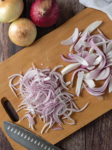 Overhead photo of red onion half with cut onion feathers on the side.