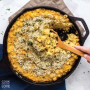 Cast iron skillet vegan baked mac and cheese on the table with spoon dipping in to serve.