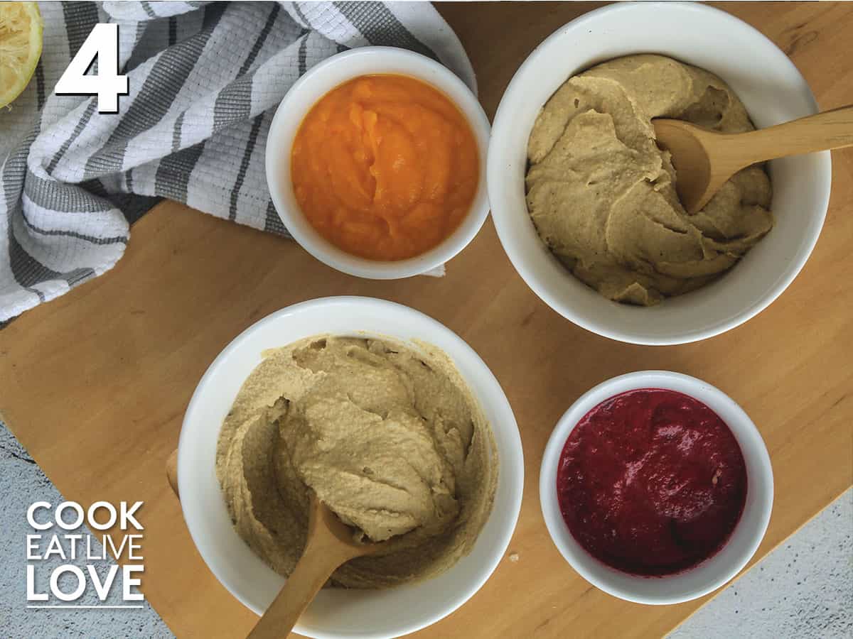 Plain hummus in bowls on cutting board with small bowls of the flavored puree