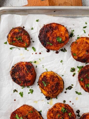 Roasted sliced sweet potatoes on a baking tray garnished with parsley.