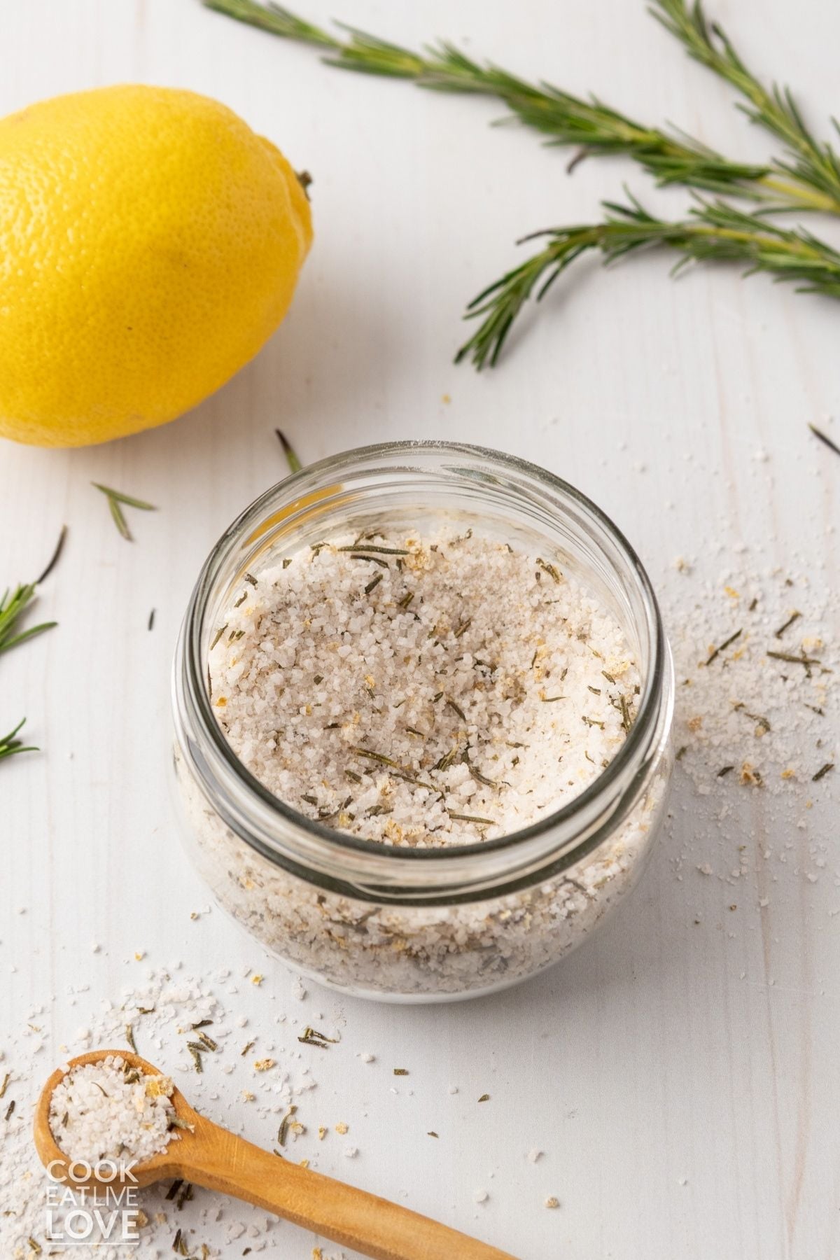 A jar of lemon rosemary salt with a lemon and fresh rosemary sprigs. 