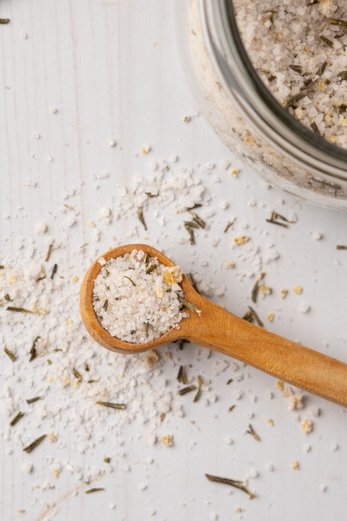 Rosemary salt in a wooden spoon and scattered on the table around it. 