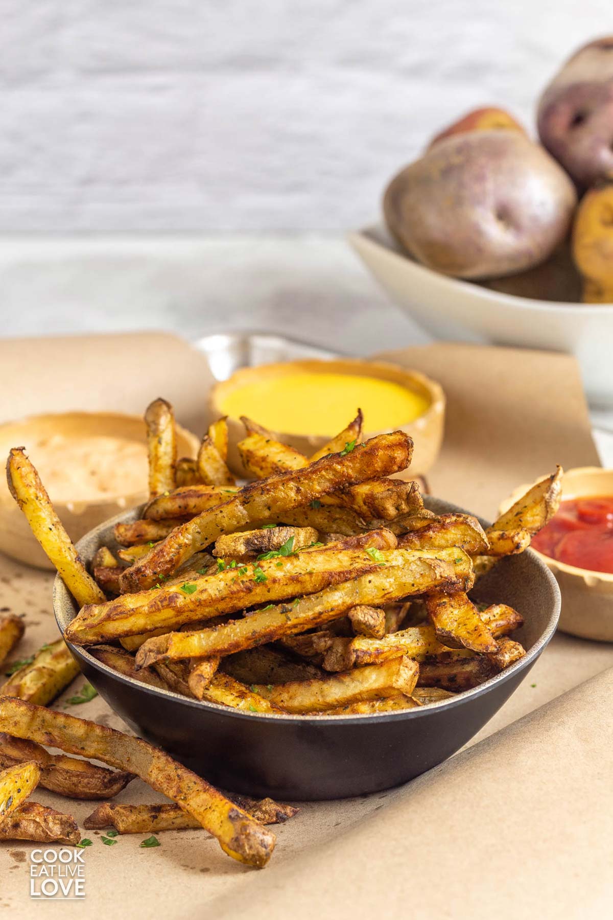Bowl of baked french fries on the table with dipping sauces.