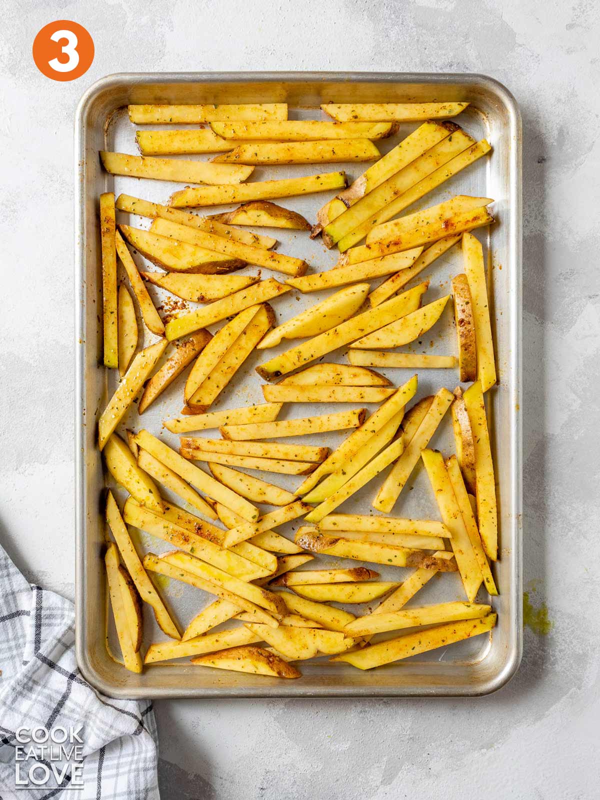 Potato strips spread out on a baking tray to make oven fries.