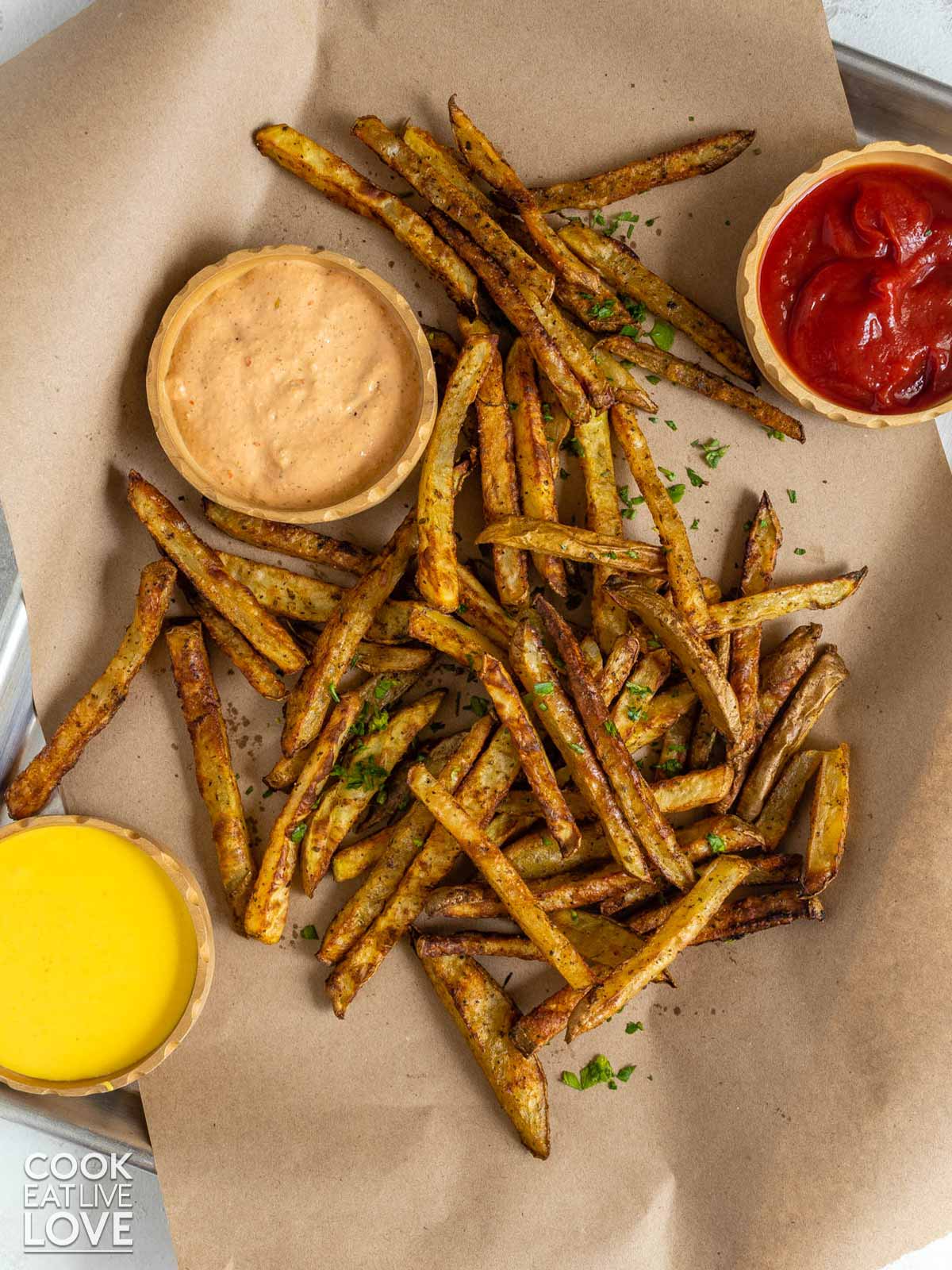 Oven fries are finished baking and served up on craft paper with sauces.
