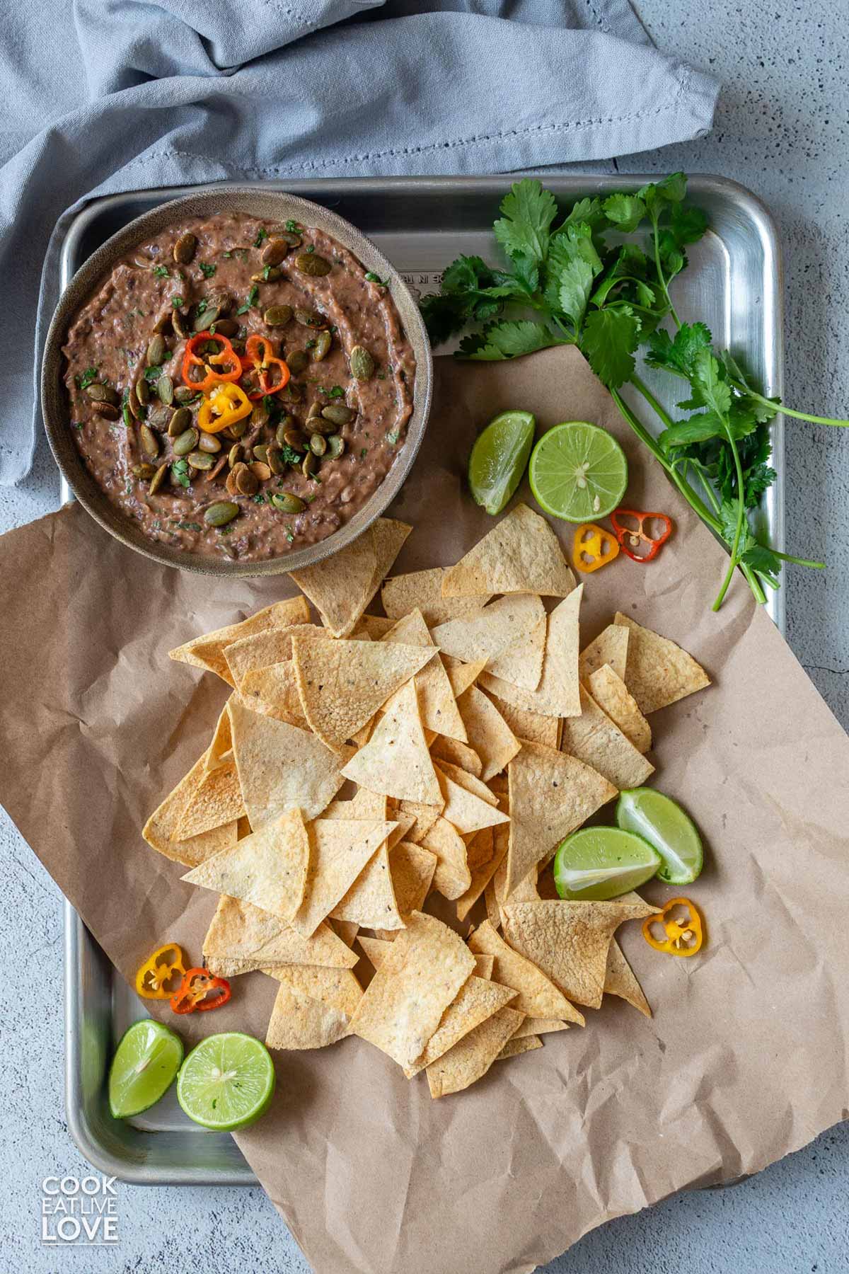 Black bean dip in a bowl with garnishes on top and served on a tray with tortilla chips.