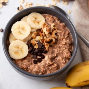 Chunky monkey overnight oats in a bowl topped with sliced bananas, walnuts, and chocolate chips.