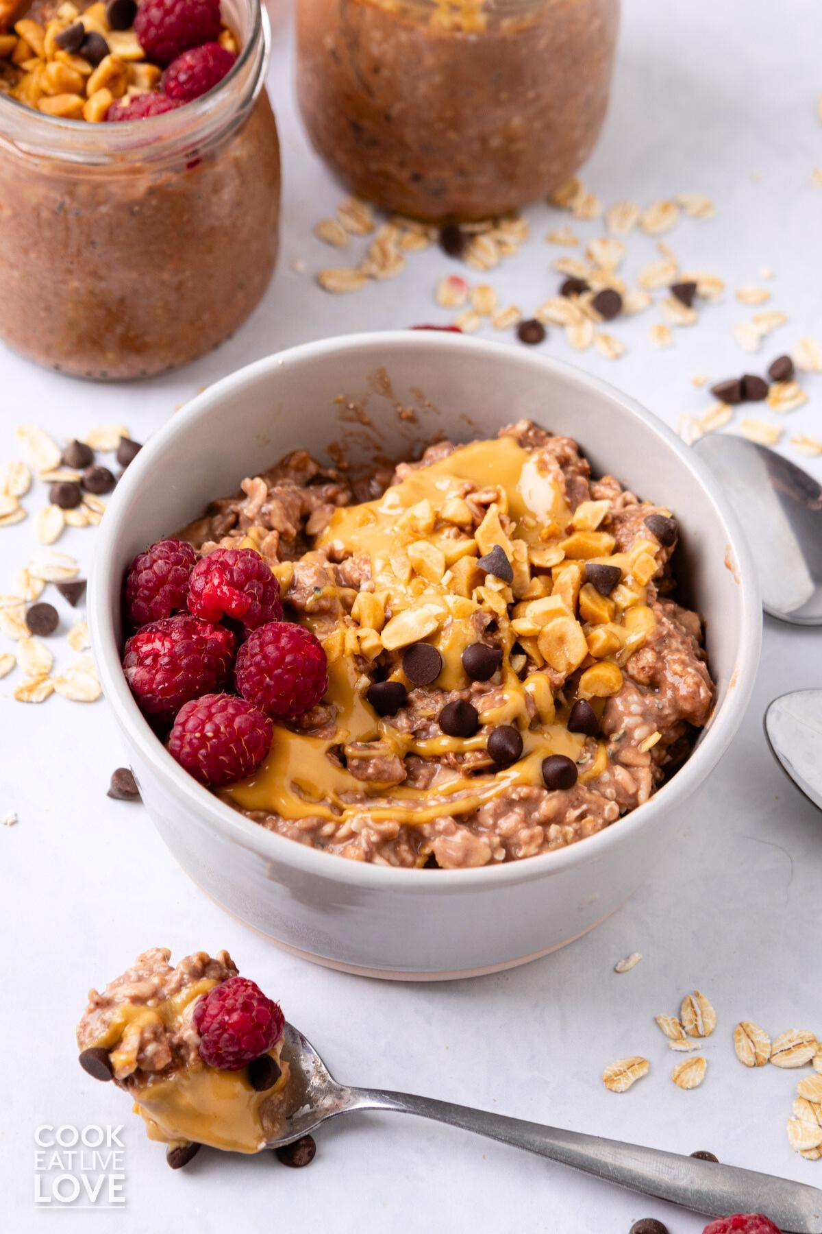 A bowl of peanut butter and jelly overnight oats on the table with a spoonful in front of the bowl.