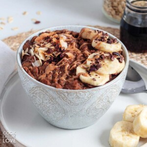 Banana chocolate oatmeal in a bowl with sliced bananas and cacao nibs on top.