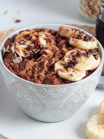 Banana chocolate oatmeal in a bowl with sliced bananas and cacao nibs on top.