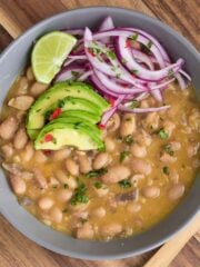 Bowl of peruvian beans on the table topped with avocado and red onion.