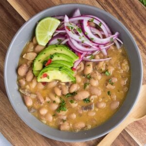 Bowl of peruvian beans on the table topped with avocado and red onion.