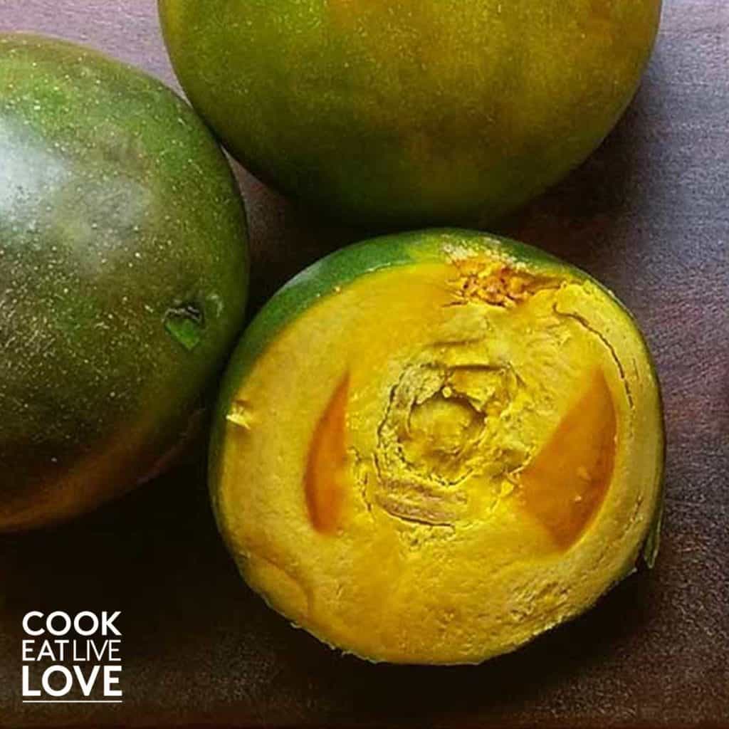 Lucuma fruit shown cut in half and whole. The whole are dark green while the flesh of the cut one is bright yellow-orange.