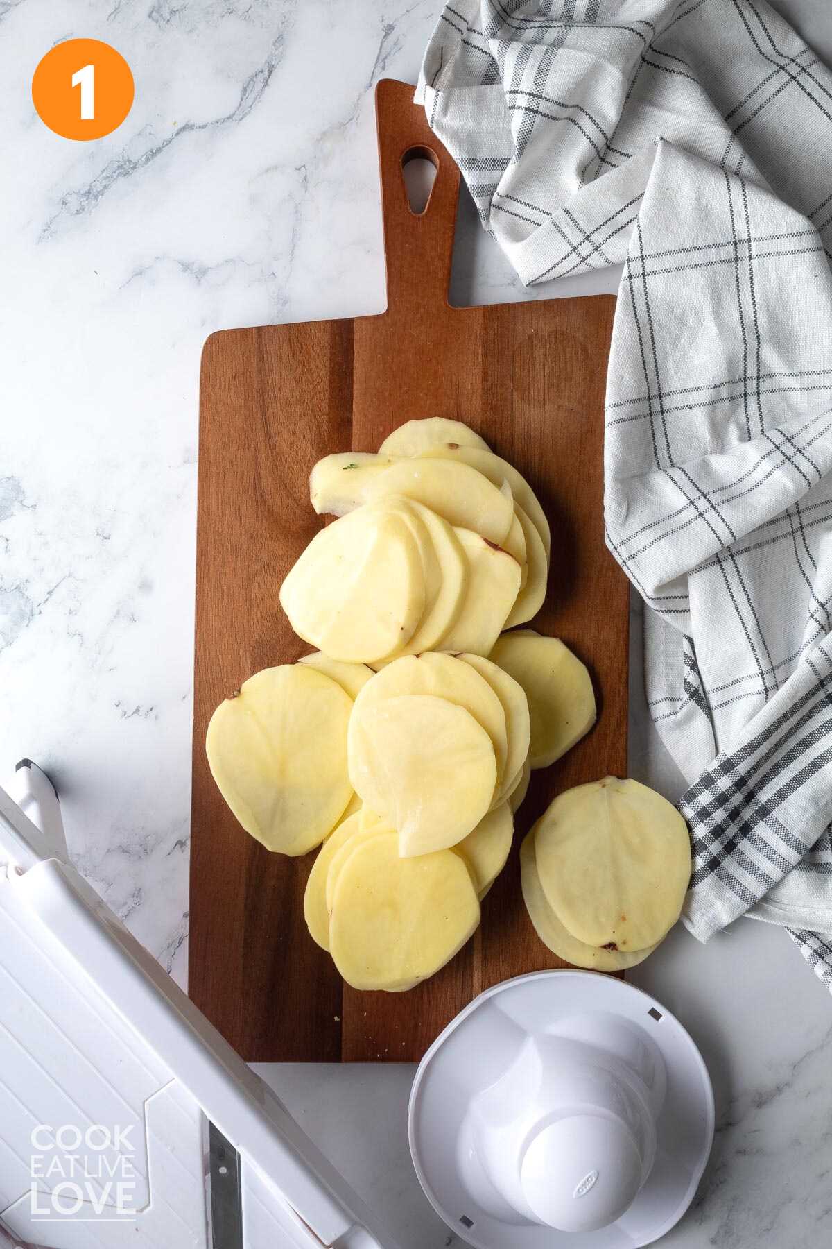 Sliced potatoes to make potato casserole on the table on a cutting board.